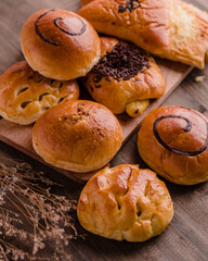Assorted sweet and savory bread rolls displayed on a rustic wooden board. The variety includes...