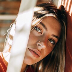 Young woman with light eyes and blond hair partially obscuring face behind white curtain, suggesting mysterious mood and subtle sensuality