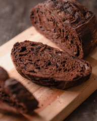Artisan chocolate bread loaf sliced on a wooden cutting board. The dark, rich interior swirled with...
