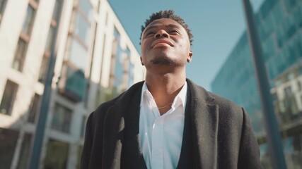 Self-confident black man standing on city street in sunny day, enjoy freedom. African american person inhaling fresh air with aroma of metropolis, dreaming about future successful, young businessman