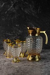 A vintage-style glass pitcher and goblet set. Ornate, textured tableware with gold trim for luxury...