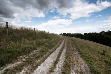 A peaceful rural scene showing a hillside path under a cloudy sky, with open views across the countryside.