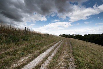 A peaceful rural scene showing a hillside path under a cloudy sky, with open views across the...