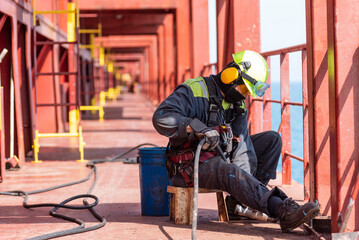 A crew member working on the deck of a merchant ship, using a pneumatic tool to remove rust.