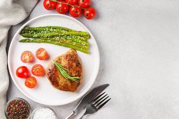 Tasty grilled beef steak served with green asparagus and cherry tomatoes on white plate, with cutlery and spices. Perfect for food menu, diet, or culinary design concepts. Top view, copy space