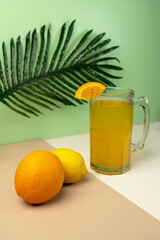 Fresh orange juice in a glass mug garnished with a slice, with a palm leaf in the background. Tropical summer drink concept with citrus fruits.