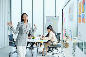 Obraz premium Happy female leader celebrating success moment with expressive gesture in light-filled office as coworkers continue collaborating on business planning.