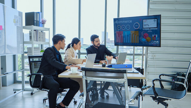 Professional Asian and multicultural team discussing performance metrics during formal meeting in office with digital marketing analytics on large screen.
