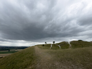 A peaceful rural scene showing a hillside path under a cloudy sky, with open views across the...