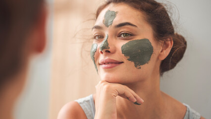Young woman applying facial mask in bathroom