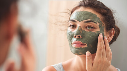 Young woman applying facial mask in bathroom