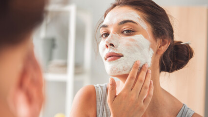Young woman applying facial mask in bathroom
