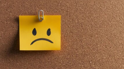 Sad emoji on a yellow sticky note symbolizes stress and frustration, pinned on a corkboard, illustrating emotions related to deadlines and time management challenges