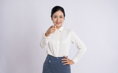 A smiling woman with confident gaze points at the viewer in front of a plain light-colored...