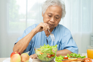 Asian elderly woman patient eating salmon steak breakfast with vegetable healthy food in hospital.