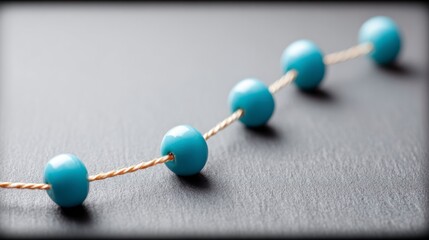 Obraz premium Five smooth light blue spherical beads threaded on a twisted tan string laid on a textured dark gray surface
