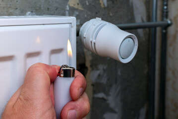 A man checks the heating of his home's radiators with a lighter.