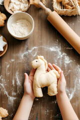 Child's hands holding a dough figure shaped like a horse on a floured wooden table. Surrounded by baking ingredients and tools. Fun and creative kids' cooking moment.
