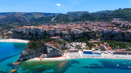 Aerial view of Tropea, Calabria, with colorful houses on a cliff overlooking the Tyrrhenian Sea, beach with umbrellas and turquoise water