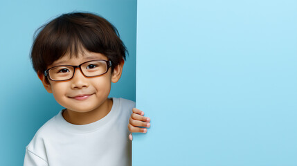 Curious little Asian toddler boy peeking around blue wall, copy space