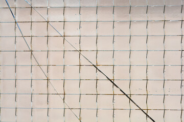 A close-up of wired glass displays a grid of embedded metal wires, with a prominent diagonal crack...