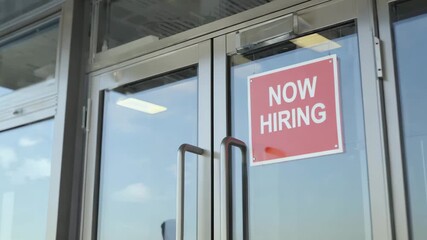 A Now Hiring sign is posted on the glass door of a business