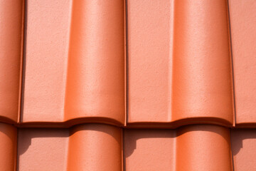 A close-up horizontal shot showcases a uniform pattern of new, reddish-brown terracotta roof tiles,...