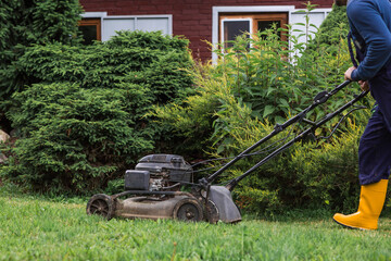 A lawn mower man mows the grass in the backyard. Agricultural machinery for garden maintenance. The...