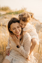 A loving mother and her happy daughter share a tender moment in sun-kissed tall grasses, both...