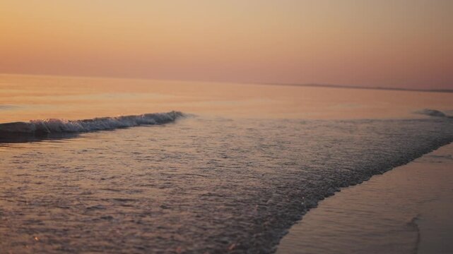 4K Slow motion shot of sea waves during the sunset at Mandvi beach in Mandvi, Kutch, Gujarat, India. Scenic view of calm beach waves of the Arabian sea during the golden hour. Water shines orange.
