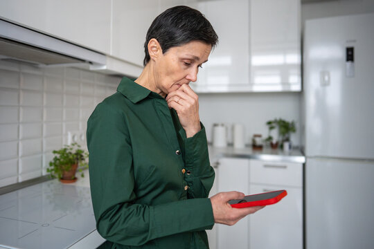 Shocked worried mature woman receiving bad news from smartphone message at home. Emotional shock, digital communication, personal crisis, mental distress, isolation, life disruption, female despair 