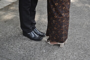 Close-up of two people standing close together, showing their feet and lower legs on a grey textured surface.