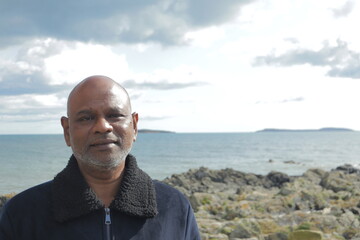 Reflective mature man gazing over calm rocky coastline under dramatic cloudy sky – peaceful...