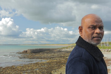 Reflective mature man gazing over calm rocky coastline under dramatic cloudy sky – peaceful...