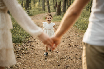 A smiling child, wearing a white dress, runs towards the camera while holding hands with her...