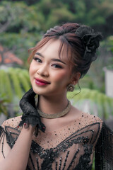 Graceful Indonesian woman wearing an elegant black kebaya with sequin embroidery and lace gloves,...