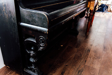 Old black piano stands in a cozy room with wooden flooring and vintage furniture