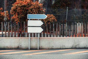 Set of three blank empty directional arrow road signs mounted on metal poles, ideal for mockups or design templates, placed against rustic wooden fence and autumn foliage background