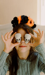 The girl holds mini Halloween skulls over her eyes.