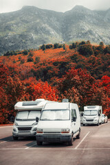 Several camper vans parked in an autumn forest lot at the foot of dramatic mountains, surrounded by vibrant red foliage and misty peaks, capturing the spirit of outdoor travel and freedom