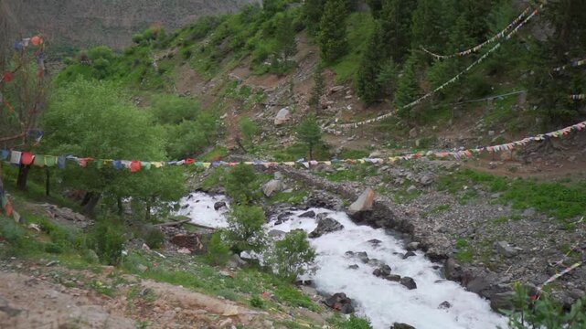 Slow motion shot of a water stream in the Himalayan mountains with prayer flags waving above it as seen near Triloknath village in Pattan valley, Himachal Pradesh, India. Scenic view of waterfall.