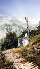 Remote telecommunications tower with orange antenna and satellite dish, enclosed by a metal fence...