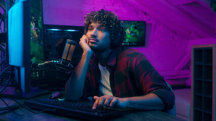 Arabian Indian bored sleepy man yawning playing game guy typing computer male takes off headphones...