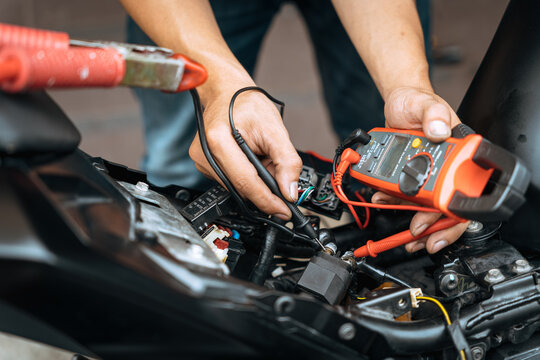 Mechanic using a multimeter check motorcycle electrical system  find wiring problems . work in garage, motorcycle repair concept ,