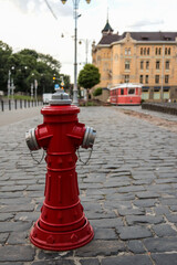 Bright red fire hydrant on a cobblestone street with a vintage red tram and historical building in...