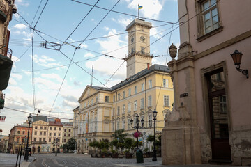 Obraz premium Scenic view of Lviv City Hall on Rynok Square with tram wires above and historical buildings around at sunset light
