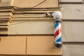 Traditional barber pole with red, white, and blue stripes mounted on an old beige wall, with...