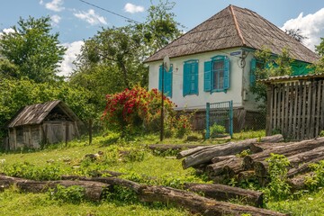 classic village house with a stack of logs in front of the gate in the village of Temnolesskaya in the Western Caucasus Mountains on a sunny summer day