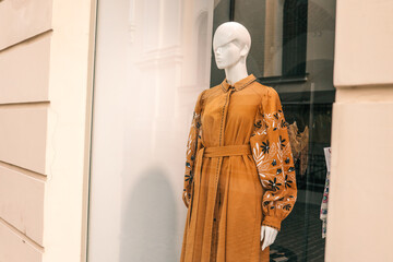 Mannequin in a shop window dressed in a mustard yellow embroidered dress with long sleeves,...