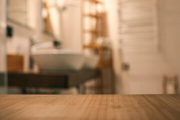 Wooden countertop in the foreground with a blurred view of a modern bathroom featuring two white...